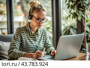 A young female freelance businessman in glasses and headphones is working on a laptop or shopping in an online store. The woman is writing something in a notebook. Стоковое AI-изображение, AI-художник Photojuli / Фотобанк Лори