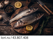 Delicious healthy fish.Raw sea bass with lemon and ingredients on a dark background. Banner, menu, place for recipe text, top view. Стоковое AI-изображение, AI-художник Photojuli / Фотобанк Лори