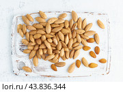Top view almonds in endocarp, bowl with drupe in shell on white wooden cutting board. Стоковое фото, фотограф Natalia Gdovskaia / Фотобанк Лори