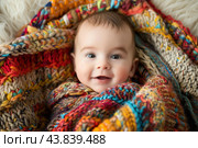 Cherubic infant snuggled in colorful blanket. Стоковое AI-изображение, AI-художник Иван Рябоконь / Фотобанк Лори