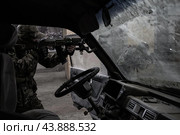 Двое военных в камуфляже целятся в противника рядом с разбитой машиной (2020 год). Редакционное фото, фотограф Евгений Зимин / Фотобанк Лори