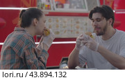 Young man and a young woman are devouring a hamburger with relish while seated alfresco. Стоковое видео, видеограф Strunov David / Фотобанк Лори