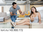 Smiling girl trying out sofa in furniture store, listening to salesman. Стоковое фото, фотограф Яков Филимонов / Фотобанк Лори