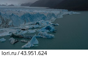 A melting glacier. A fragment. A wall of blue cracked ice rises above a turquoise glacial lake. Melted ice floes float in the water. The mountains are in a fog. Perito Moreno. Argentina. El Calafate. Стоковое фото, фотограф Вера Ивановна Кубарева / Фотобанк Лори