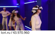 Four cheerful emotional young female friends in VR goggles standing in virtual reality room, manipulating objects or shooting at targets with gaming controllers in hands. Стоковое видео, видеограф Яков Филимонов / Фотобанк Лори