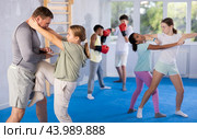 Tween girl performing knee strike in midsection to instructor in self-defense sparring. Стоковое фото, фотограф Яков Филимонов / Фотобанк Лори