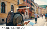 A happy male tourist in a hat with a backpack, holding a map and exploring a European city on a sunny day. Стоковое AI-изображение, AI-художник Tatiana Syrtseva / Фотобанк Лори