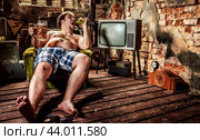 Fat man eating a hamburger sitting on a chair in the slums. Стоковое фото, фотограф Андрей Армягов / Фотобанк Лори
