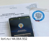 Телефон с электронным приложением налоговой службы "Налоги ФЛ" и Налоговая декларация 3 - НДФЛ (2024 год). Редакционное фото, фотограф Татьяна Т / Фотобанк Лори