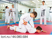 Two boys in kimonos train to perform painful grips during karate training in gym under the guidance of female trainer. Стоковое фото, фотограф Яков Филимонов / Фотобанк Лори