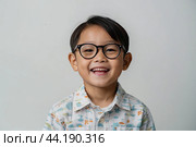 Portrait of a happy Asian kid schoolboy with glasses on a solid gray background. Back to school, correction of pupil kid eyesight. AI generated. Стоковое AI-изображение, AI-художник Ольга Симонова / Фотобанк Лори