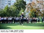 Старшеклассник несёт на плече первоклассницу и они звонит в колокольчик на 1й звонок в школе (2019 год). Редакционное фото, фотограф Оксана / Фотобанк Лори