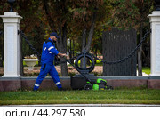 Рабочий стрижет траву в парке у Северного речного вокзала летним днем в городе Москве, Россия (2024 год). Редакционное фото, фотограф Николай Винокуров / Фотобанк Лори