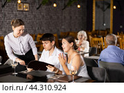 Waitress helps to sort out menu, choose original dish to young married couple. Стоковое фото, фотограф Яков Филимонов / Фотобанк Лори