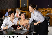 Waitress helps to sort out menu, choose original dish to young married couple. Стоковое фото, фотограф Яков Филимонов / Фотобанк Лори
