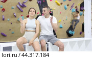 Two friendly climbers, young girl and guy, taking break between climbs at indoor bouldering gym, sitting and discussing next routes and technique in casual conversation. Стоковое видео, видеограф Яков Филимонов / Фотобанк Лори