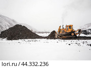 Бульдозер в горной местности сгребает кучу горного золотосодержащего грунта , который в дальнейшем будет перевозиться на промывку с целью извлечения желтого драгоценного метала. Стоковое фото, фотограф Павел Просянов / Фотобанк Лори