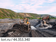 Американский бульдозер CATERPILLAR в горной местности, сгребает от промывочного устройства отработанный горный грунт, чтобы затем его сгрести ковшом в отвал. На дальнем плане - стационарное промывочное устройство для промывки золота (2010 год). Редакционное фото, фотограф Павел Просянов / Фотобанк Лори