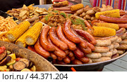 Огромная сковорода, в которой лежат мясные колбаски из разных сортов мяса, овощи, обжаренные на гриле и картофель фри на гастрономическом фестивале в Парке 300-летия Санкт-Петербурга (2024 год). Стоковое фото, фотограф Елена Яворская / Фотобанк Лори
