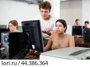 Smart teen schoolboy helping cute girl classmate sitting at computer during informatics lesson. Стоковое фото, фотограф Яков Филимонов / Фотобанк Лори