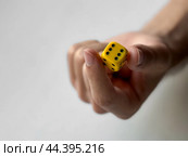 Close-up of hand holding yellow dice with black dots on minimalist background. Стоковое фото, фотограф Lamina Akulova / Фотобанк Лори