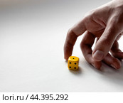Hand rolling yellow dice on white surface for luck and strategy. Стоковое фото, фотограф Lamina Akulova / Фотобанк Лори