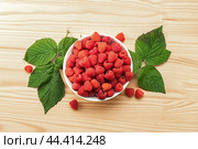 Raspberries on white plate on wooden table with leaves. Organic raspberries grown without use of chemical fertilizers and pesticides. Raspberries on wooden background. top view. Стоковое фото, фотограф Павел Муравьев / Фотобанк Лори