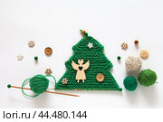 Merry Christmas and Happy New Year. Hand knitted green wool Christmas tree is decorated with buttons, beads and wooden angel. Balls of woolen yarn and knitting needle nearby. Empty space for text. Стоковое фото, фотограф Виктория Катьянова / Фотобанк Лори