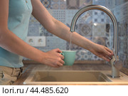 The young woman pours water from the kitchen faucet. Стоковое фото, фотограф Ольга Петрова-Апостолова / Фотобанк Лори