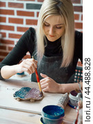 Woman making pattern on ceramic plate with paint brush. Creative hobby concept. Earn extra money, side hustle, turning hobbies into cash, passion into job, vertical. Стоковое фото, фотограф Natalia Gdovskaia / Фотобанк Лори