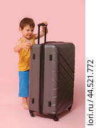 A young boy drags his luggage, eager for a vacation full of fun, studio pink background. Kid aged three years (a three-year-old boy) Стоковое фото, фотограф Андрей Журавлев / Фотобанк Лори