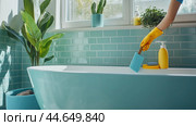 A person cleans a modern turquoise bathtub with bright yellow gloves in a sunny, green indoor space filled with plants. Стоковое AI-изображение, AI-художник Сергей Толмачёв / Фотобанк Лори