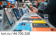 Customer comparing smartphones in electronics store. Стоковое AI-изображение, AI-художник Юрий Поздников / Фотобанк Лори