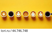 Various hot coffees in ceramic cups lined up on a yellow background. Стоковое AI-изображение, AI-художник Veniamin Kraskov / Фотобанк Лори