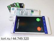 Смартфон, телефон, мобильник с неизвестным входящим звонком на фоне денег и банковских карт. Smartphone, phone, mobile with an unknown incoming call against a backdrop of money and bank cards (2024 год). Редакционное фото, фотограф Юрий Пуликов / Фотобанк Лори