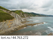 Breathtaking seascape in Basque Autonomous Community / country in gloomy summer day. Atlantic ocean beach Algorri surrounded by mountains at low tide in Bay of Biscay. Layers of flysch on the coast at Zumaia. Стоковое фото, фотограф YuryKara / Фотобанк Лори