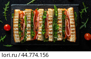 Grilled sandwich with fresh vegetables and melty cheese on a wooden cutting board. Стоковое AI-изображение, AI-художник Юлия Гапеенко / Фотобанк Лори
