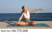 Woman performs half-lotus pose with torso tilted to sides at sea embankment. Стоковое видео, видеограф Яков Филимонов / Фотобанк Лори
