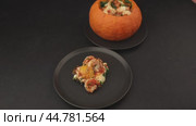 Whole baked pumpkin with tiger prawns, melted cheese and tomatoes. A woman places a dish on a plate. Traditional dish of Brazil, home cooking. Selective focus, close-up, black background. Стоковое видео, видеограф Наталья Любина / Фотобанк Лори