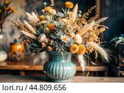 A beautiful bouquet of dried flowers in a ceramic vase on an antique wooden chest of drawers. A bouquet of flowers in a vase in a home interior. Light, beige, blue floral background. Стоковое AI-изображение, AI-художник Photojuli / Фотобанк Лори