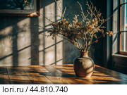 Branches with golden autumn leaves in a ceramic vase on a wooden table by the window. The concept of home comfort. Autumn decor for Halloween. Стоковое AI-изображение, AI-художник Photojuli / Фотобанк Лори
