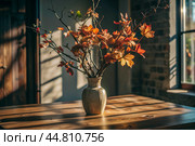 Branches with golden autumn leaves in a ceramic vase on a wooden table by the window. The concept of home comfort. Autumn decor for Halloween. Стоковое AI-изображение, AI-художник Photojuli / Фотобанк Лори