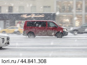 Red Volkswagen Transporter T5 minibus riding at winter city street during snowfall. Редакционное фото, фотограф Константин Григорьев / Фотобанк Лори