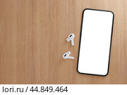 Modern smartphone with blank white screen with wireless earphones on wooden table. Mockup TWS earbuds with smartphone on wood background. copy space. Стоковое фото, фотограф Павел Муравьев / Фотобанк Лори