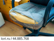 Aging office chair bears the scars of time, with its frayed covering exposing the soft foam beneath. This image speaks to the weariness of work life and the stories held in forgotten furniture. Стоковое фото, фотограф Татьяна Степанищева / Фотобанк Лори