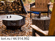 Eco-friendly, stylish barbecue area and wooden chairs for relaxing by the campfire. An axe will be stuck into a wooden log. Chopping firewood. Стоковое фото, фотограф Photojuli / Фотобанк Лори