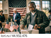 President elections. A black man votes for the new president of the United States of America and puts a form in the ballot box against the background of the American flag. Стоковое AI-изображение, AI-художник Photojuli / Фотобанк Лори