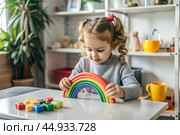 Toys. A little girl is playing educational games. A rainbow-shaped children's toy, colored pyramids and logic toys for children. Montessori games for child development. Стоковое AI-изображение, AI-художник Photojuli / Фотобанк Лори