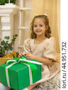 Christmas spirit. Happy little smiling girl is sitting in the children room in a tent and opening Christmas gifts. Happy girl unwrapping Christmas present box. Holidays and celebrations concept. Стоковое фото, фотограф Ирина Михайличенко / Фотобанк Лори
