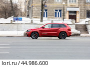 Fast moving Jeep Grand Cherokee on the city road. Red SUV with man driving. Premium auto in fast motion with blurred background. Speeding in the city concept. Редакционное фото, фотограф Константин Григорьев / Фотобанк Лори
